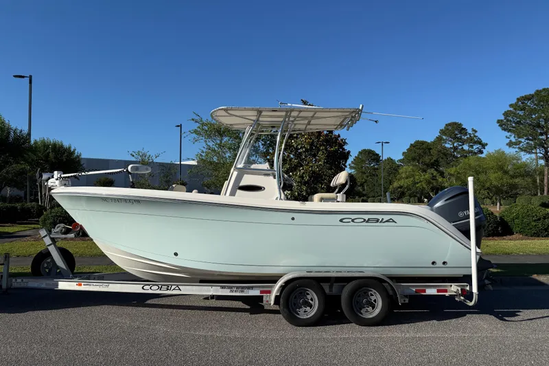 The Image of 2018 Cobia 220 Center Console boat on trailer, parked outdoors under clear blue sky. - 1