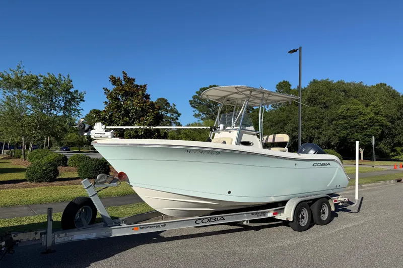 Slide: The Image of 2018 Cobia 220 Center Console boat on trailer, parked outdoors under clear blue sky. - 2