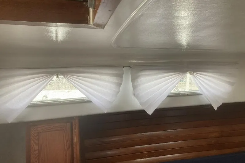 Slide: The Image of Interior of a 1974 Ericson 32-2 sailboat with white curtains and wooden seating. - 23