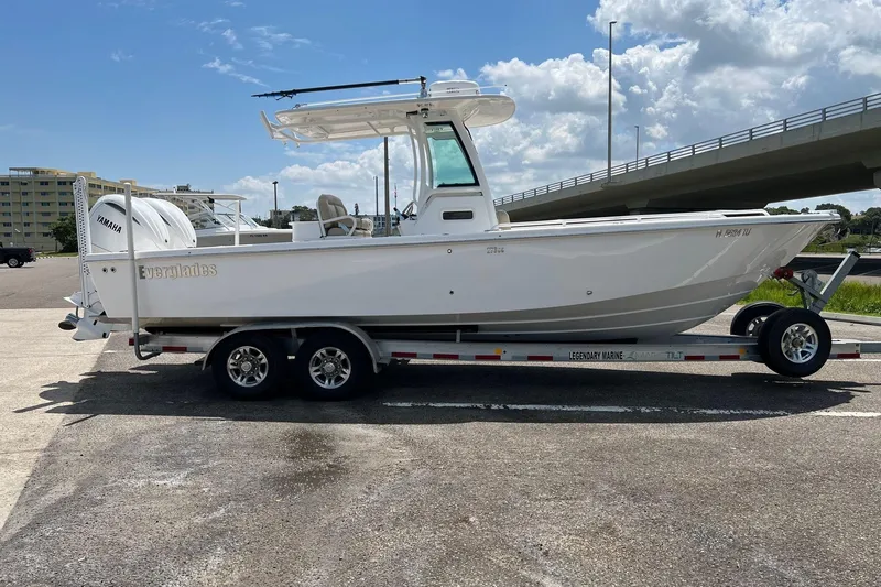 Slide: The Image of 2019 Everglades 273 Center Console boat on trailer, parked near a bridge under a blue sky. - 21