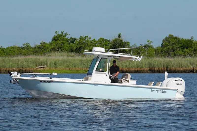 Slide: The Image of 2019 Everglades 273 Center Console boat cruising on a calm lake with lush greenery. - 7