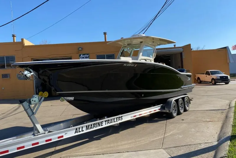 Slide: The Image of 2015 Scout 320 LXF boat on trailer outside a garage, sunny day. - 11