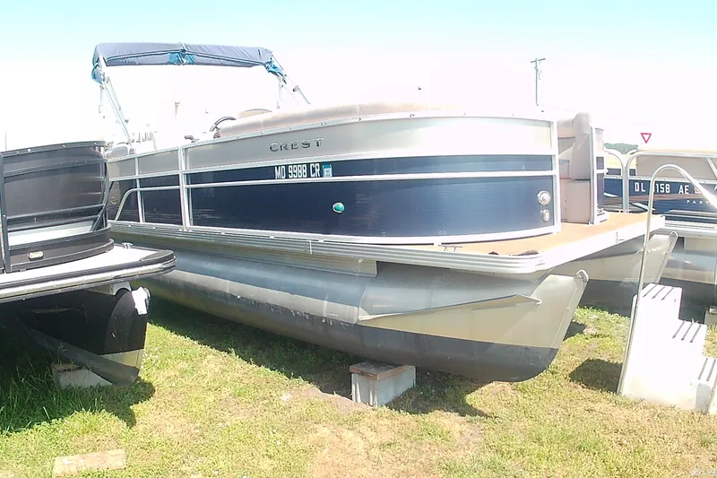 Slide: The Image of 2015 Crest 230 bar pontoon boat on grass, featuring sleek design and blue accents. - 2