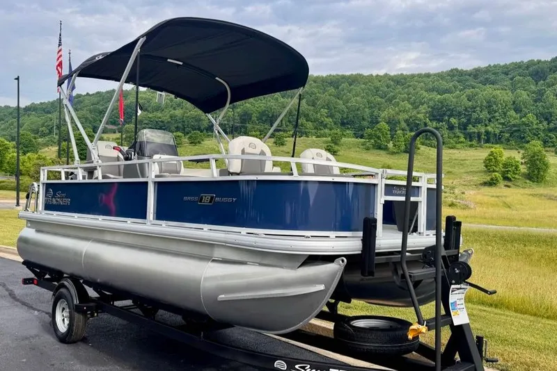 Slide: The Image of 2026 Sun Tracker Bass Buggy 18 DLX pontoon boat on trailer, scenic background. - 2
