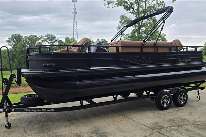 Slide: The Image of 2026 Ranger 223F pontoon boat on trailer, parked outdoors with lush greenery. - 4