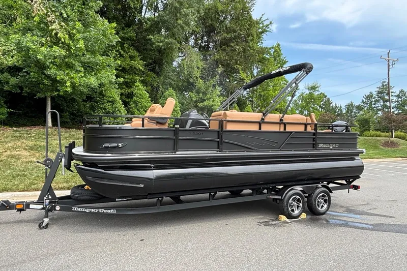 Slide: The Image of 2026 Ranger 220F pontoon boat on trailer, parked in a lot with trees in background. - 1