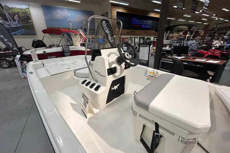 Slide: The Image of 2026 Mako Pro Skiff 15 CC boat displayed in showroom with steering console and seating. - 4