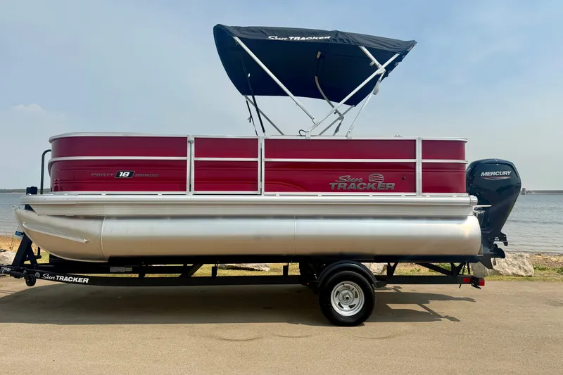The Image of 2026 Sun Tracker Party Barge 18 DLX pontoon boat on trailer by the water. - 0