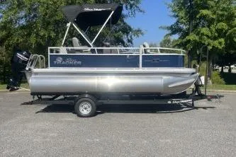 Slide: The Image of 2026 Sun Tracker Bass Buggy 16 XL Select pontoon boat on trailer, parked outdoors. - 2