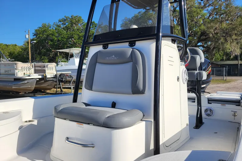 Slide: The Image of 2023 NauticStar 227 XTS boat interior with seating and console, parked outdoors. - 6