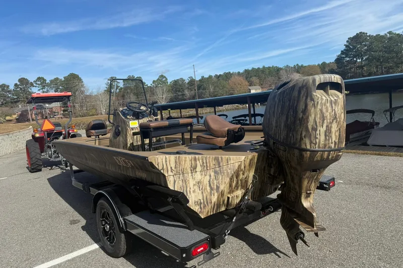 Slide: The Image of Camouflage-patterned 2026 Excel 206 Stalker CC boat on trailer, parked near a lake. - 2