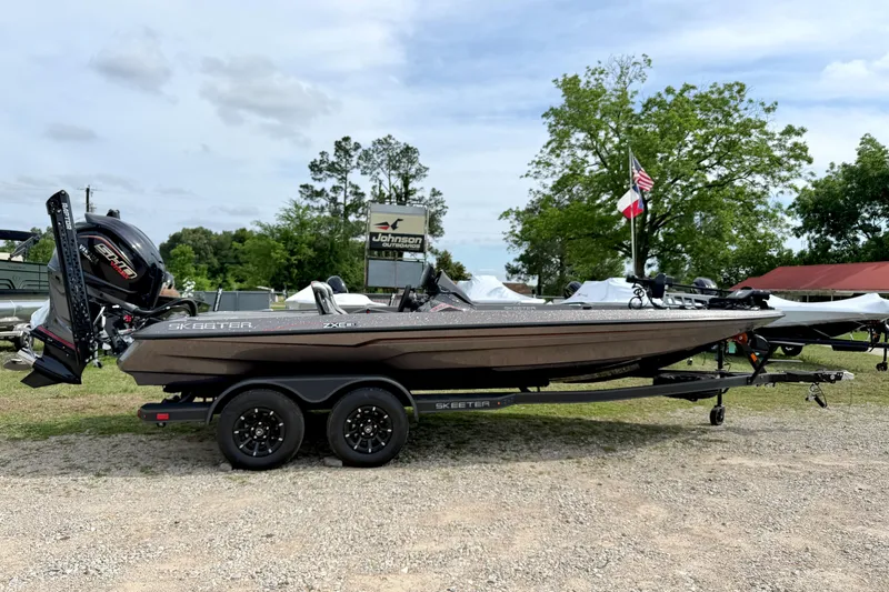The Image of 2026 Skeeter ZXE21 boat on trailer, displayed outdoors with trees and flags in the background. - 0