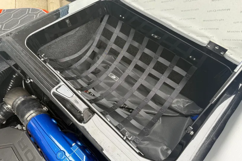 Slide: The Image of 2025 MasterCraft NXT23 boat storage compartment with netting and visible engine components. - 24