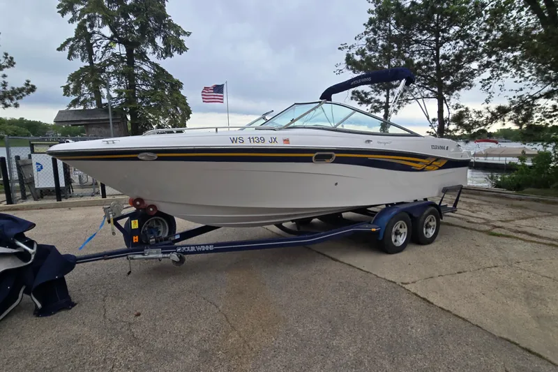 Slide: The Image of 2001 Four Winns 230 Horizon boat on trailer, parked near a lake with trees and American flag. - 2