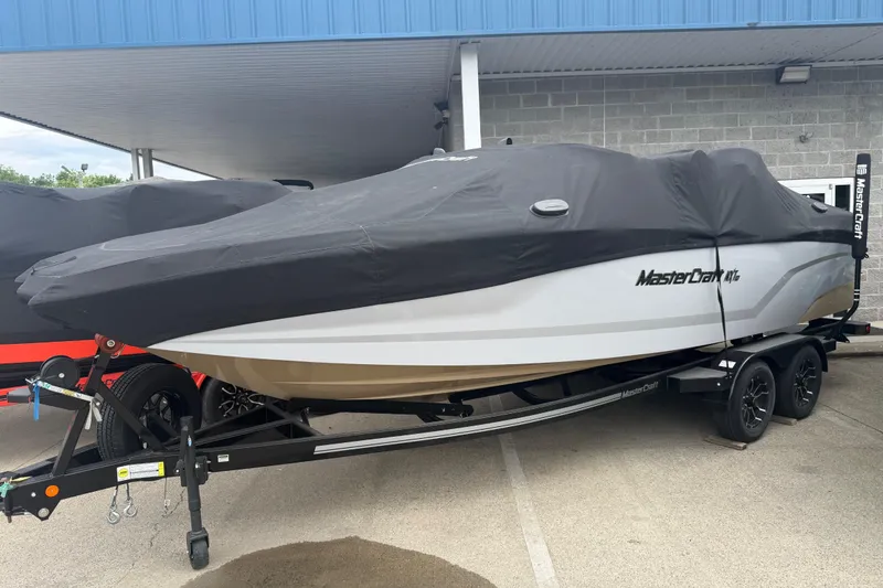 Slide: The Image of 2025 MasterCraft NXT24 boat covered, on trailer, parked outdoors. - 2