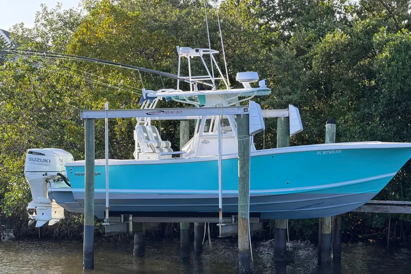 The Image of 2002 Regulator 26 Center Console boat with Suzuki engine on a lift by the water. - 1