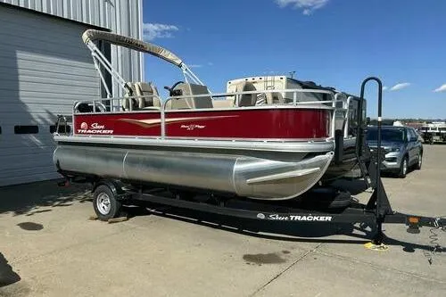 The Image of 2025 Sun Tracker Bass Buggy 18 DLX pontoon boat on trailer, parked outdoors. - 1