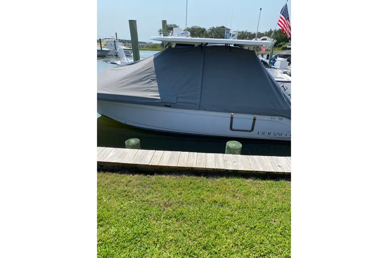 Slide: The Image of 2021 Robalo R272 Center Console boat docked with cover, grassy foreground. - 5