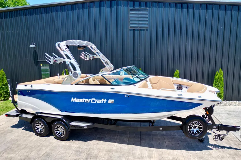 The Image of 2020 MasterCraft XT22 boat with blue and white exterior on a trailer. - 1