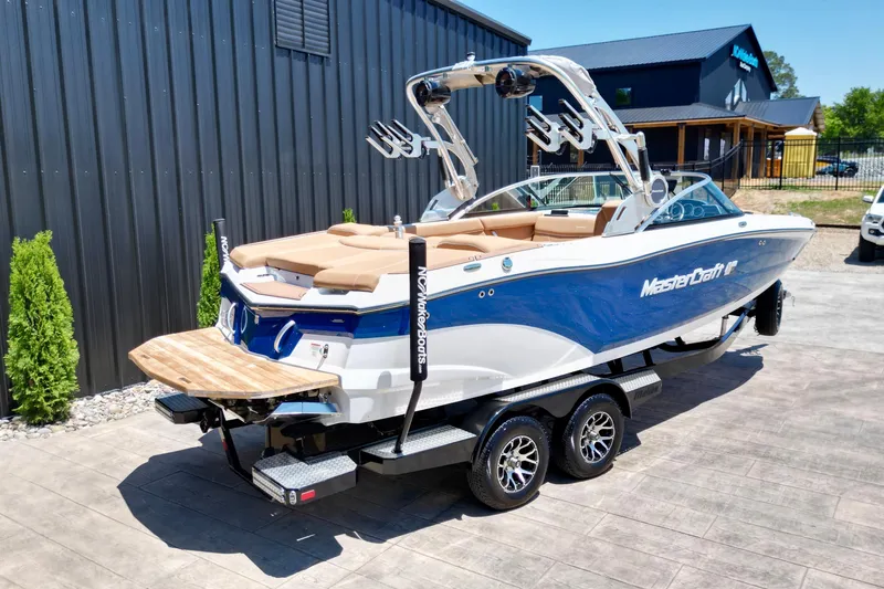 Slide: The Image of 2020 MasterCraft XT22 boat on trailer, blue and white design, parked outdoors. - 15