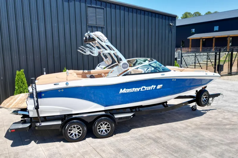Slide: The Image of 2020 MasterCraft XT22 boat in blue and white on a trailer, parked outdoors. - 3
