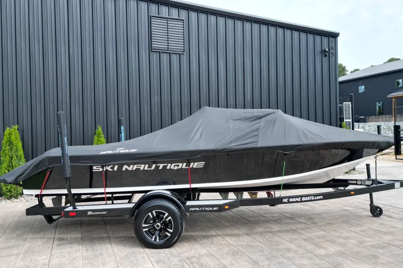 Slide: The Image of 1994 Nautique Ski Nautique boat covered on trailer, parked by black building. - 19