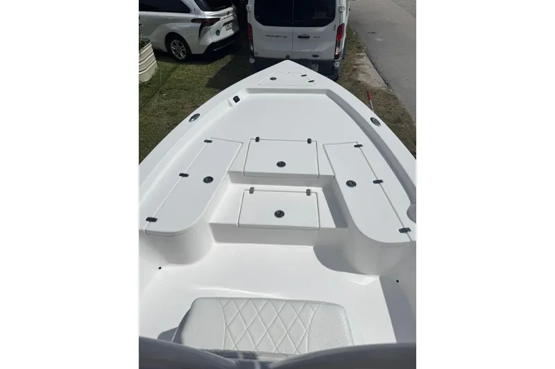 Slide: The Image of 2024 Blazer Bay 2220 Fisherman boat deck with storage compartments, parked near vehicles. - 3