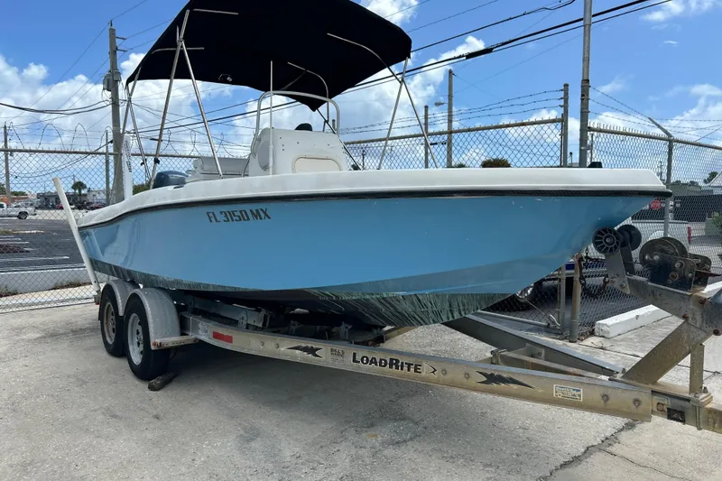 The Image of 2004 HYDRASPORT 20 boat on trailer, blue hull, parked near chain-link fence. - 0