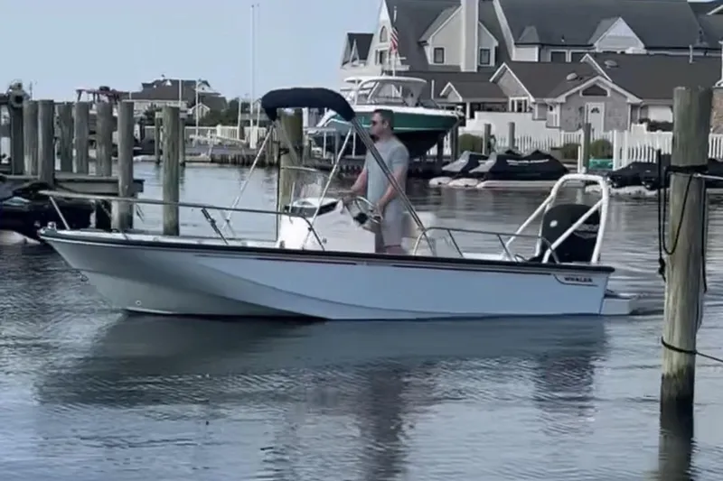 Slide: The Image of 2025 Boston Whaler 170 Montauk boat cruising in a marina with waterfront homes. - 2