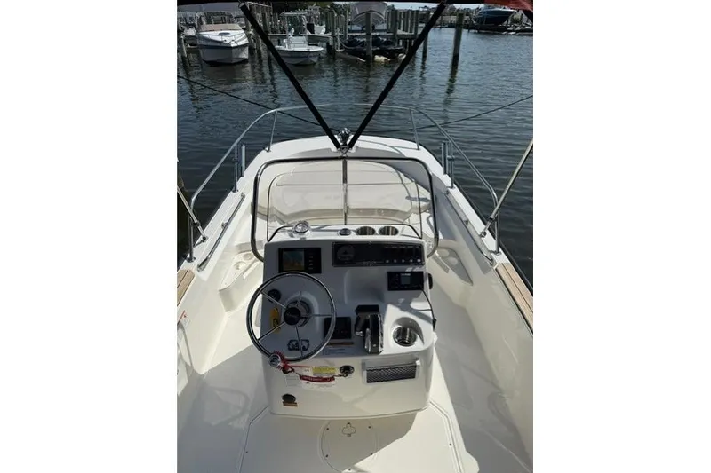 Slide: The Image of 2025 Boston Whaler 170 Montauk boat interior with steering wheel and controls, docked at marina. - 4