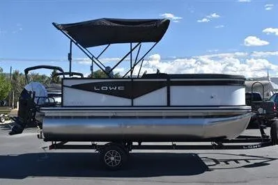 The Image of 2025 Lowe LS 170 pontoon boat with canopy on trailer, parked outdoors. - 0