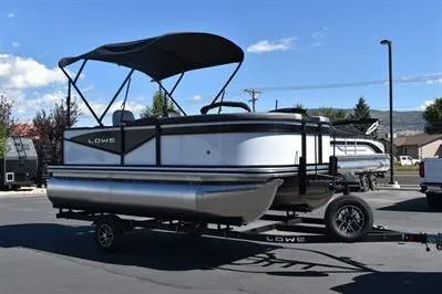 Slide: The Image of 2025 Lowe LS 170 pontoon boat on trailer under clear blue sky. - 2