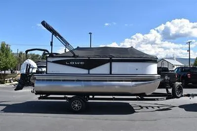 Slide: The Image of 2025 Lowe LS 170 pontoon boat on trailer, parked outdoors under a blue sky. - 6
