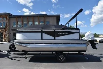 Slide: The Image of 2025 Lowe LS 170 pontoon boat on trailer, parked outdoors under blue sky. - 7