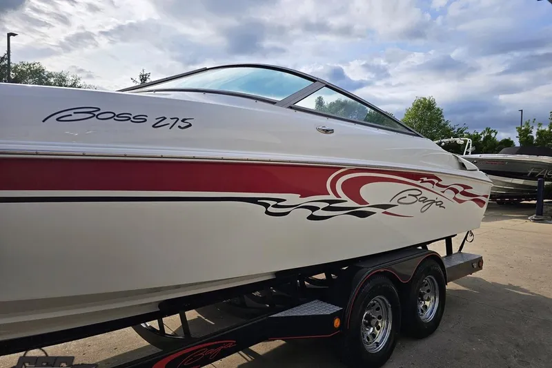 Slide: The Image of 2004 Baja 275 boat with red and black graphics on a trailer, parked outdoors. - 18