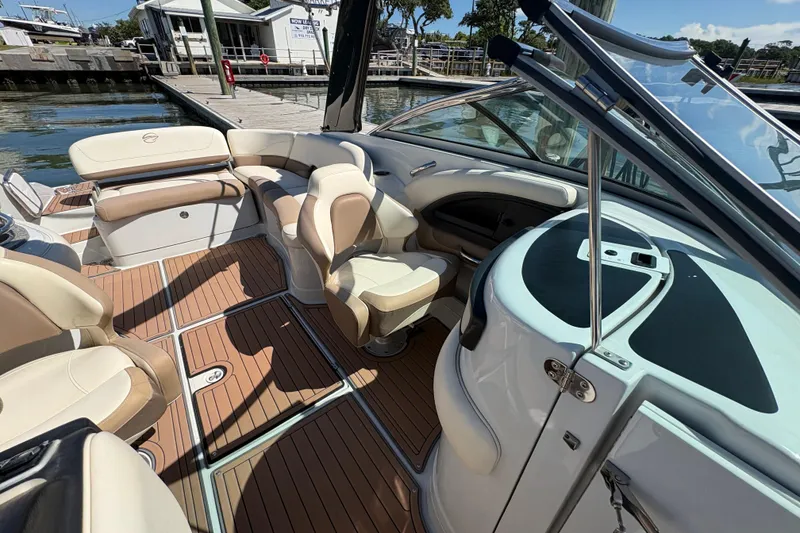 Slide: The Image of 2017 Crownline 275 SS boat interior with beige seating and wood flooring at a marina. - 16