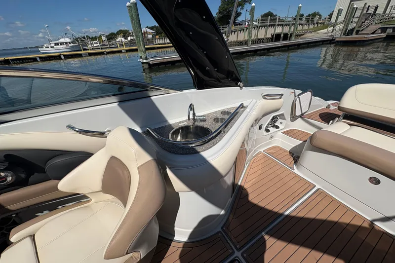 Slide: The Image of 2017 Crownline 275 SS boat interior with seating, sink, and wood-style flooring at a marina. - 23