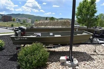 The Image of 2024 Lowe L1240 Jon boat on display outdoors, surrounded by greenery and mountains. - 0