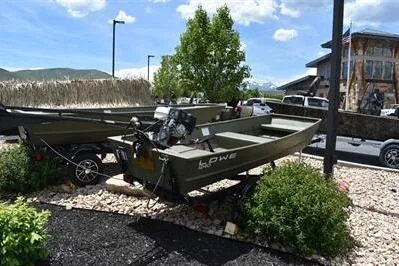 Slide: The Image of 2024 Lowe L1240 Jon boat displayed outdoors with motor, surrounded by greenery. - 2