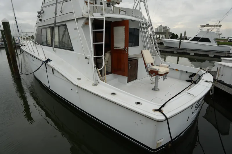 The Image of 1980 Hatteras 50 Convertible yacht docked at marina, featuring spacious deck and fishing chair. - 2