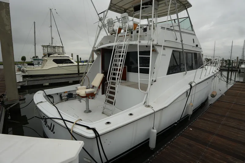 Slide: The Image of 1980 Hatteras 50 Convertible yacht docked at marina, featuring spacious deck and fishing chair. - 4