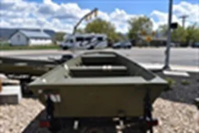 Slide: The Image of 2024 Lowe L1448M Jon boat on display outdoors, with a trailer and clear sky background. - 2