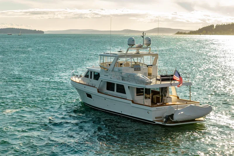 Slide: The Image of 2023 Offshore Yachts 64 ELV cruising on a sunlit ocean with scenic coastline. - 50