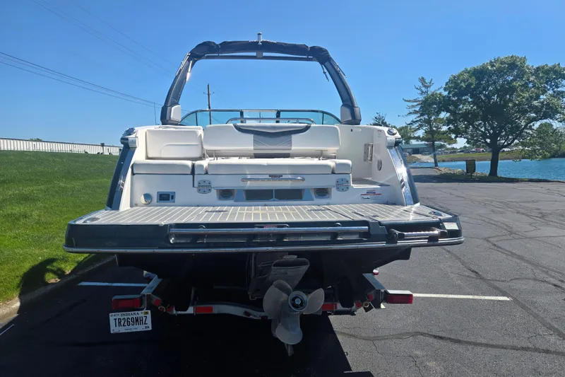 Slide: The Image of 2018 Chaparral 267 SSX boat rear view, parked near a lake on a sunny day. - 2
