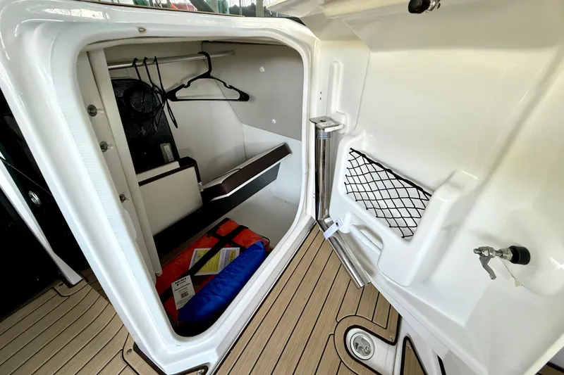 Slide: The Image of 2022 Yamaha Boats 252SD storage compartment with hangers and life jackets on teak flooring. - 22
