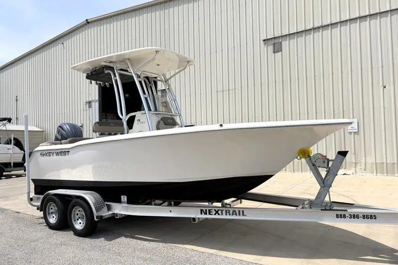Slide: The Image of 2024 Key West 203 FS boat on trailer, parked outside a large warehouse. - 2