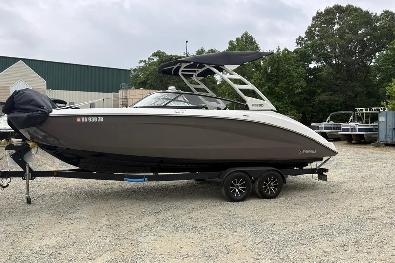 The Image of 2023 Yamaha Boats 252SD on trailer, parked outdoors, with trees and buildings in the background. - 1