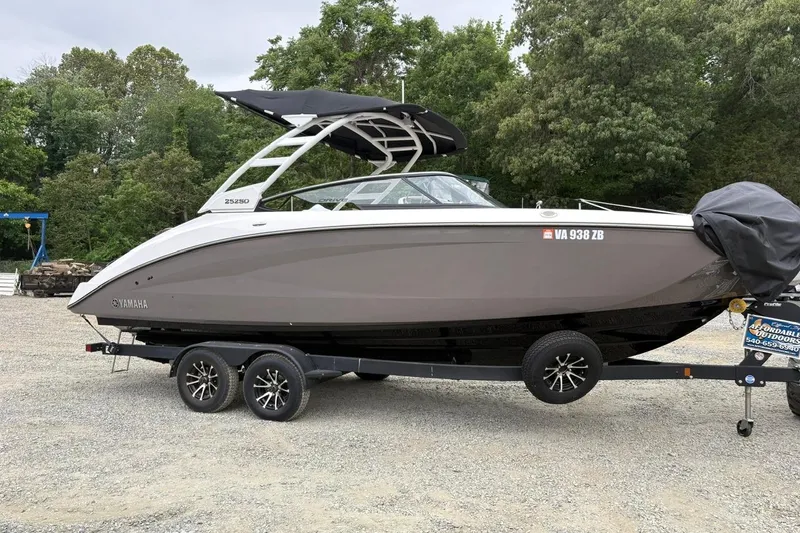 Slide: The Image of 2023 Yamaha Boats 252SD on trailer, parked outdoors with trees in background. - 2