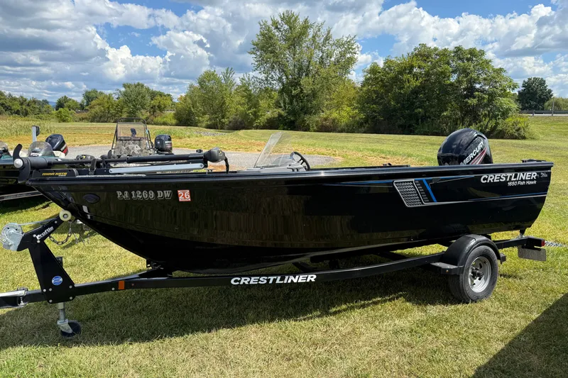The Image of 2018 Crestliner 1650 Fish Hawk SC boat on trailer, parked on grass under a cloudy sky. - 0