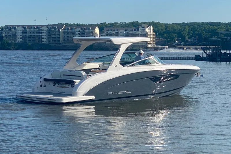 The Image of 2021 Regal 3300 Bowrider cruising on a serene lake with waterfront buildings in the background. - 0